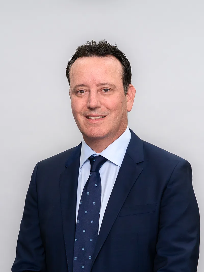 Corporate headshot of a man in a navy suit and tie against a gray studio backdrop