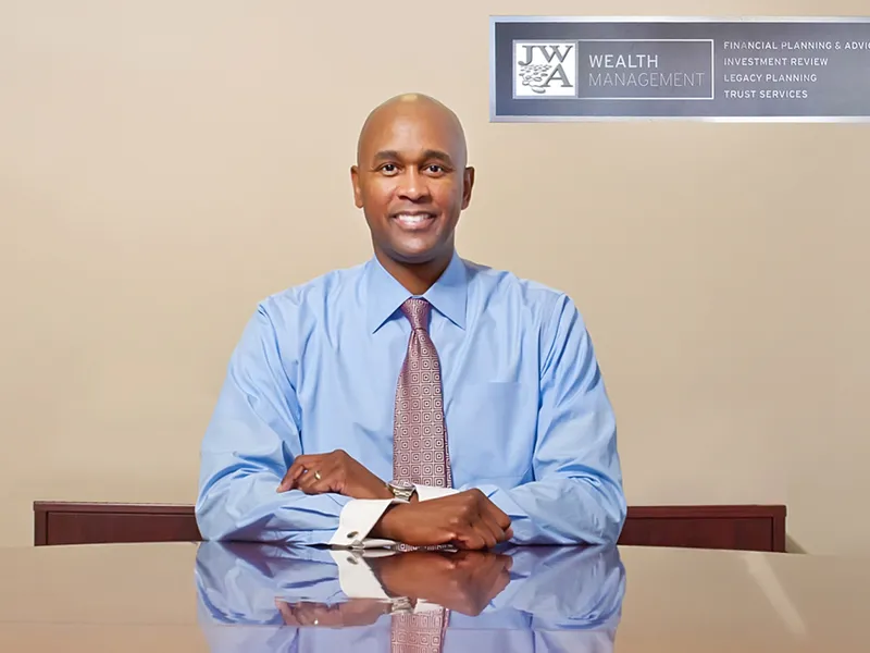 Corporate headshot of a man in a blue dress shirt and tie seated at a conference table