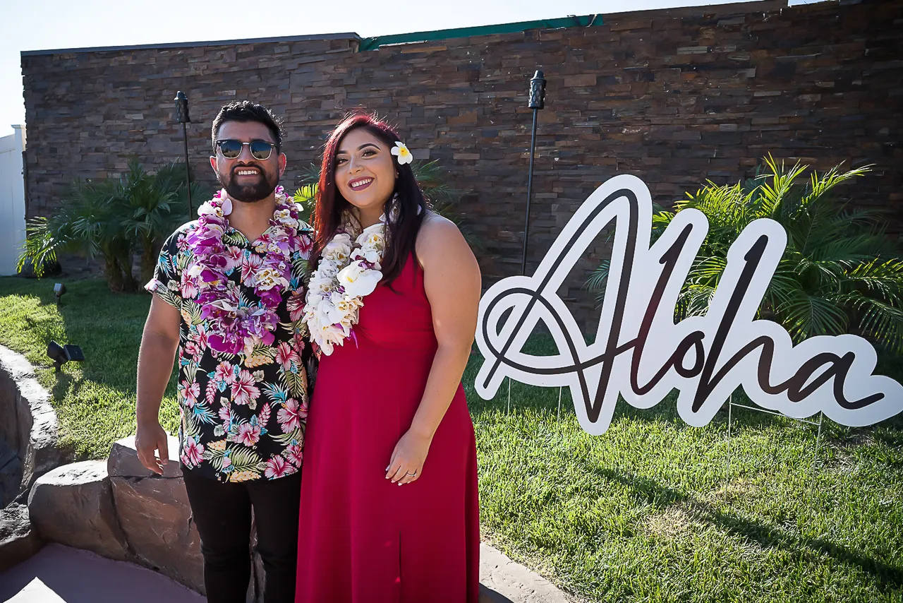 Couple standing next to a tropical-themed party welcome sign