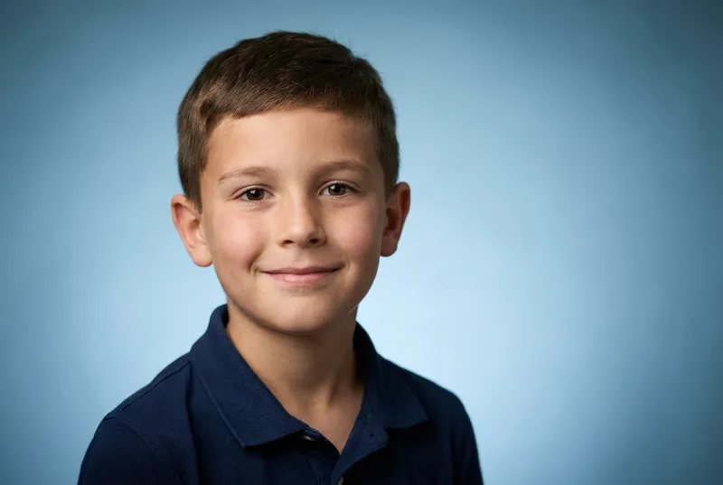 Boy in a navy polo shirt smiling against a blue backdrop