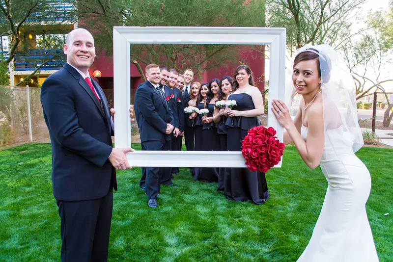 Bride and groom holding a large picture frame around their smiling wedding party on the lawn