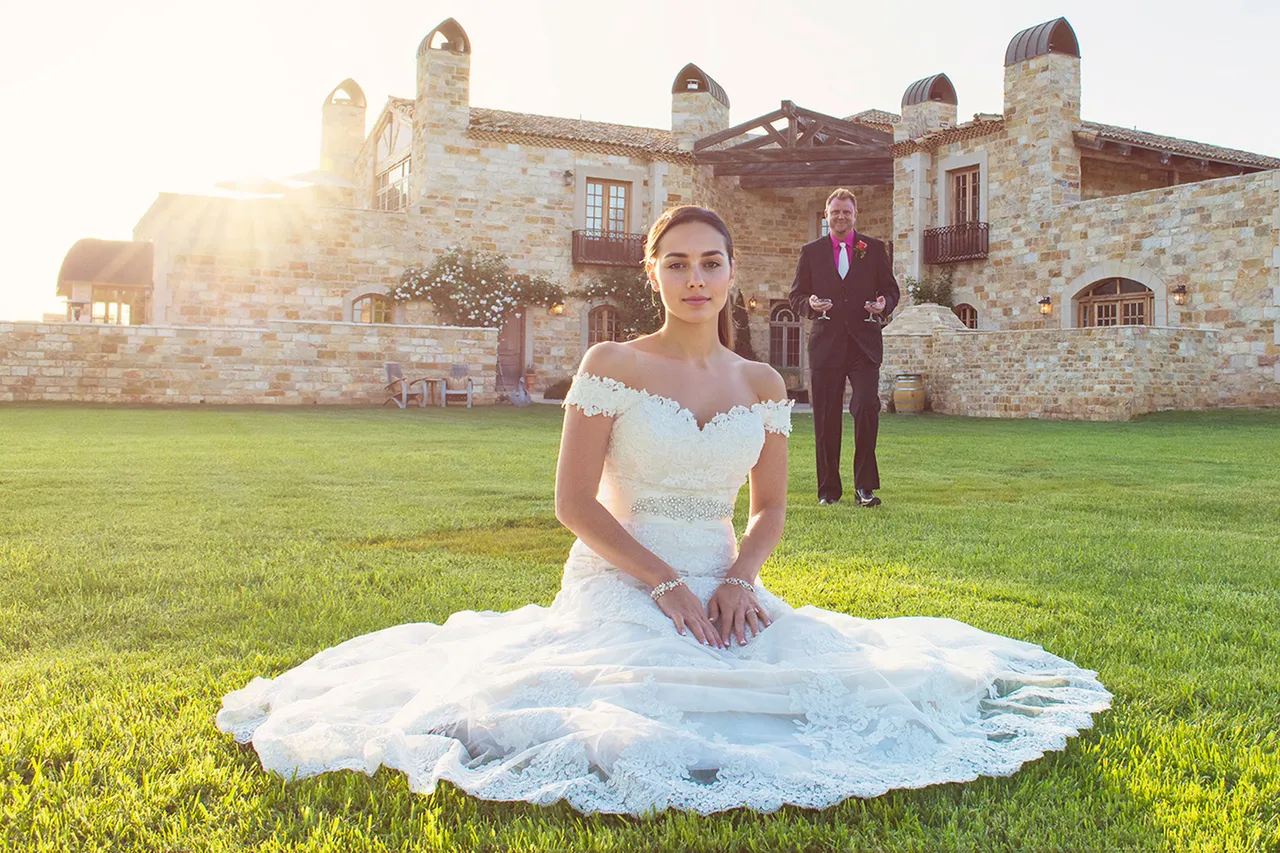 Bride seated on the lawn with groom approaching, estate building behind them, Sunstone Winery near Solvang