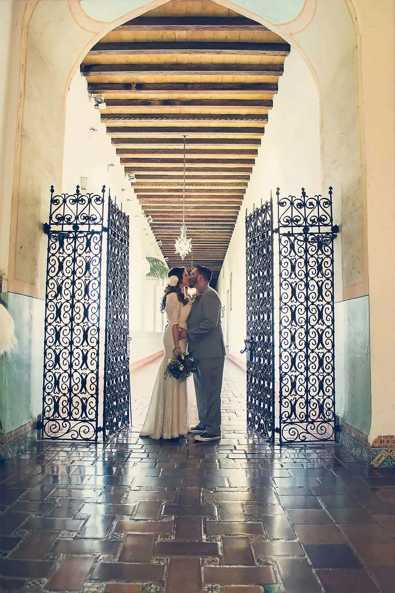 Couple kissing under an ornate archway with iron gates, Santa Barbara