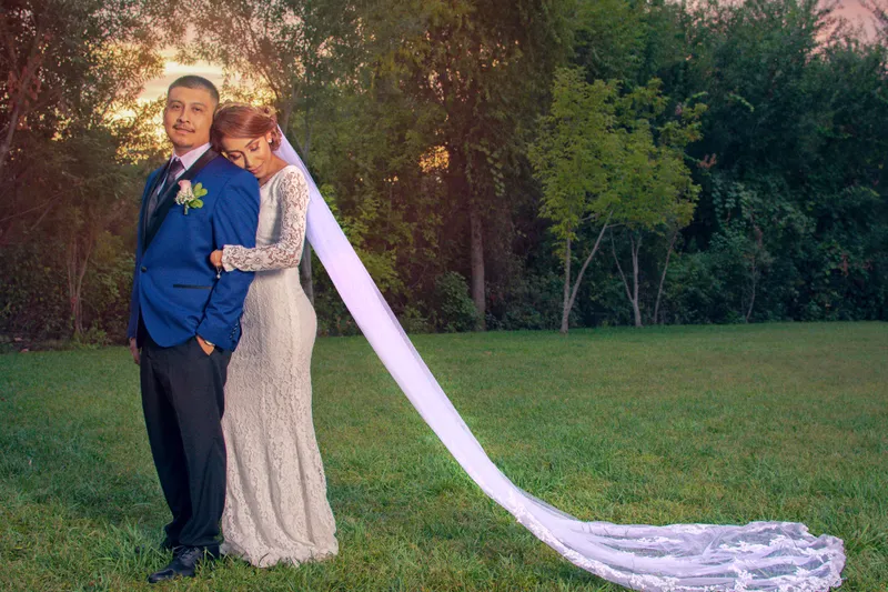 Groom in a blue jacket with the bride's long cathedral veil flowing at golden hour