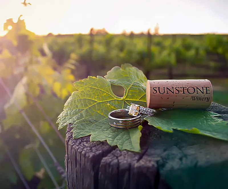Two rings resting on a grape leaf beside a branded wine cork